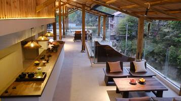 Um interior moderno com uma longa mesa de jantar, área de estar e grandes janelas com vista para o exterior.