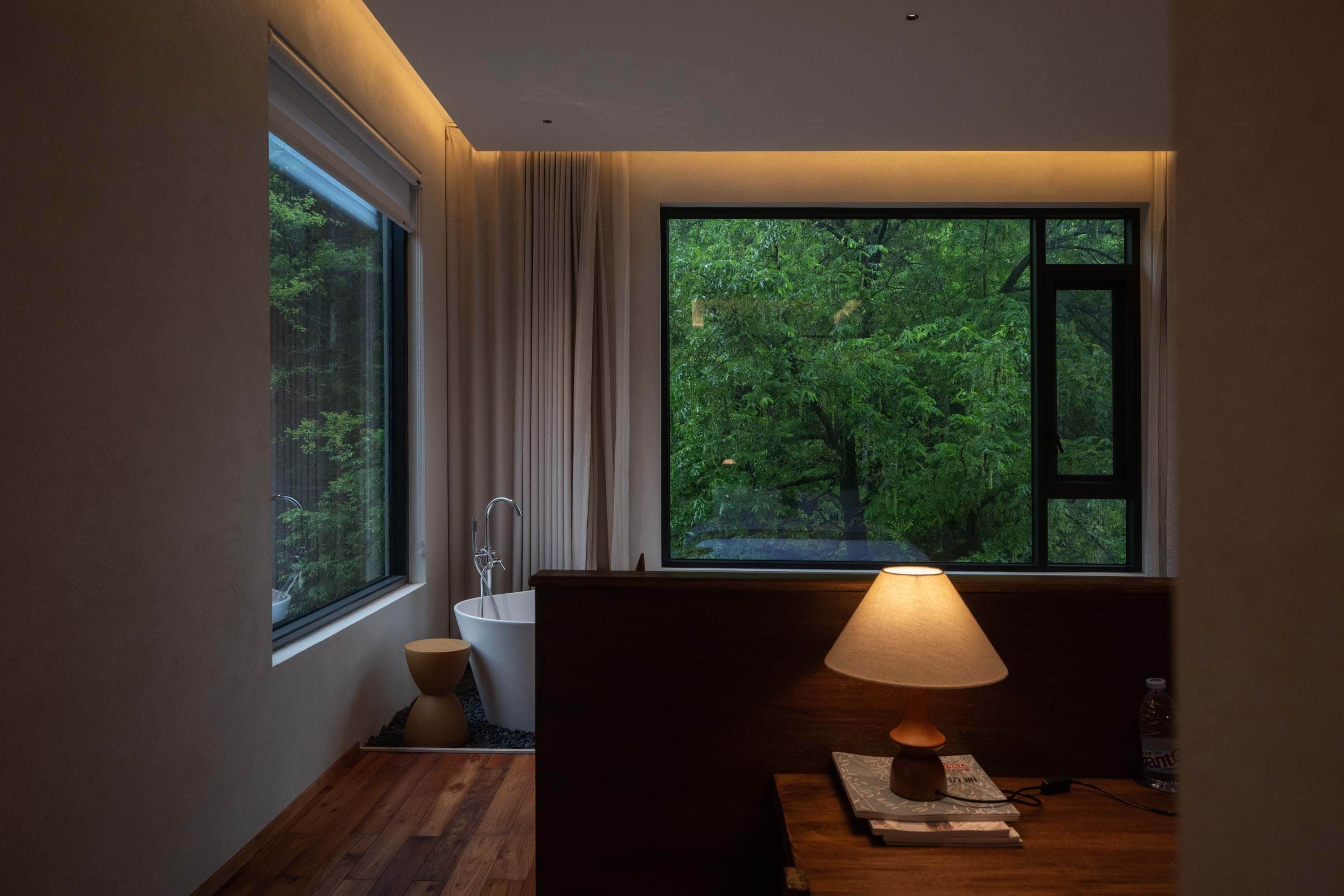 A modern bathroom with a bathtub, a toilet, and a window offering a view of a forest.
