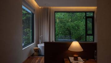 A modern bathroom with a bathtub, a toilet, and a window offering a view of a forest.