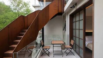 Un interior moderno con una escalera, barandilla de cristal y una zona de estar con mesas y sillas.