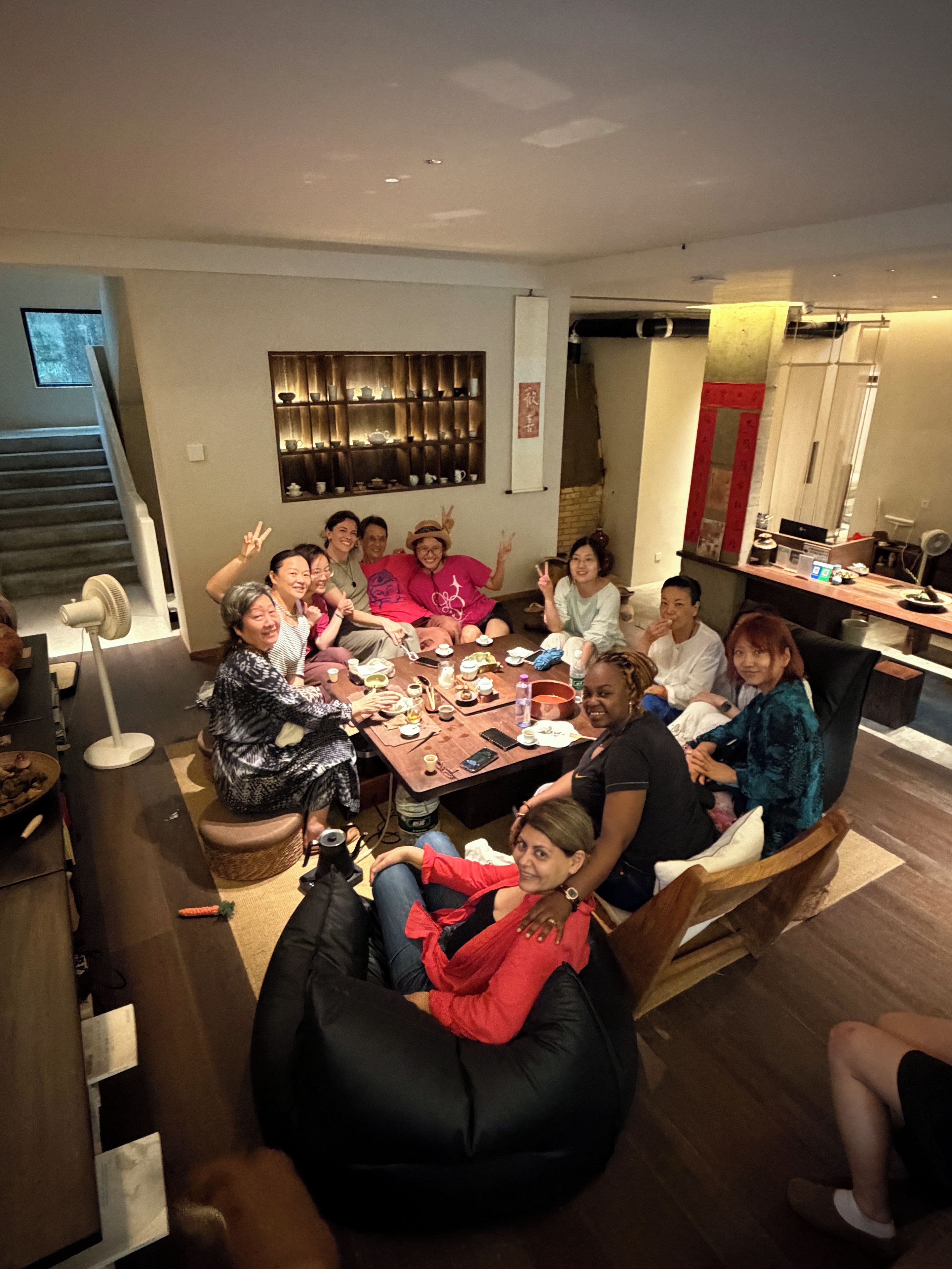Un grupo de personas sentadas alrededor de una mesa en una habitación con una escalera y una zona de cocina.