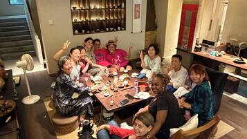 Un grupo de personas sentadas alrededor de una mesa en una habitación con una escalera y una zona de cocina.