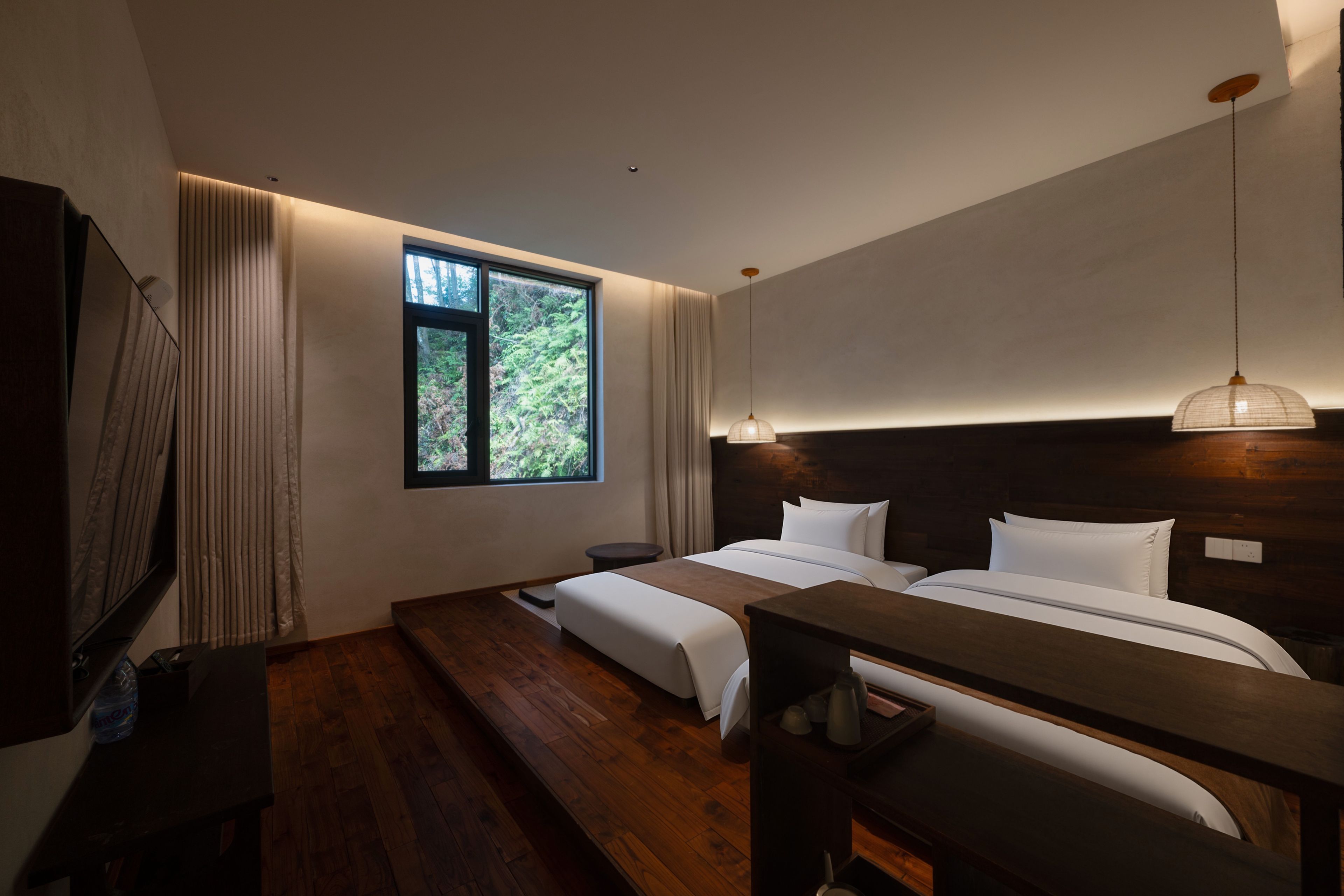 Una habitación de hotel moderna con una cama grande, una mesita de noche pequeña, un escritorio y una ventana con vistas a zonas verdes.