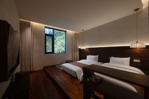Una habitación de hotel moderna con una cama grande, una mesita de noche pequeña, un escritorio y una ventana con vistas a zonas verdes.