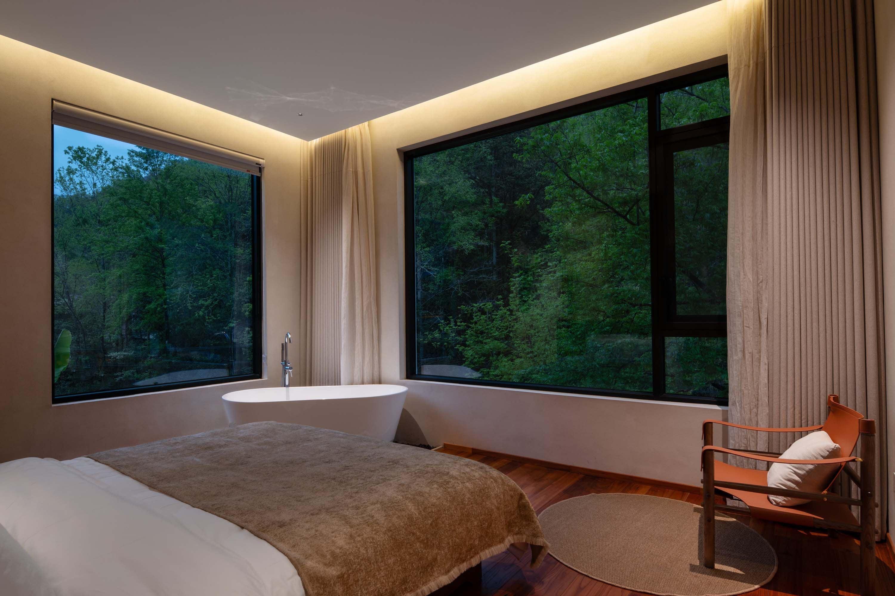 A modern bedroom with a large window, a bathtub, and a wooden floor.