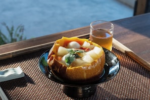 Un tazón de sopa con verduras y un vaso de té sobre una mesa con vista al mar.
