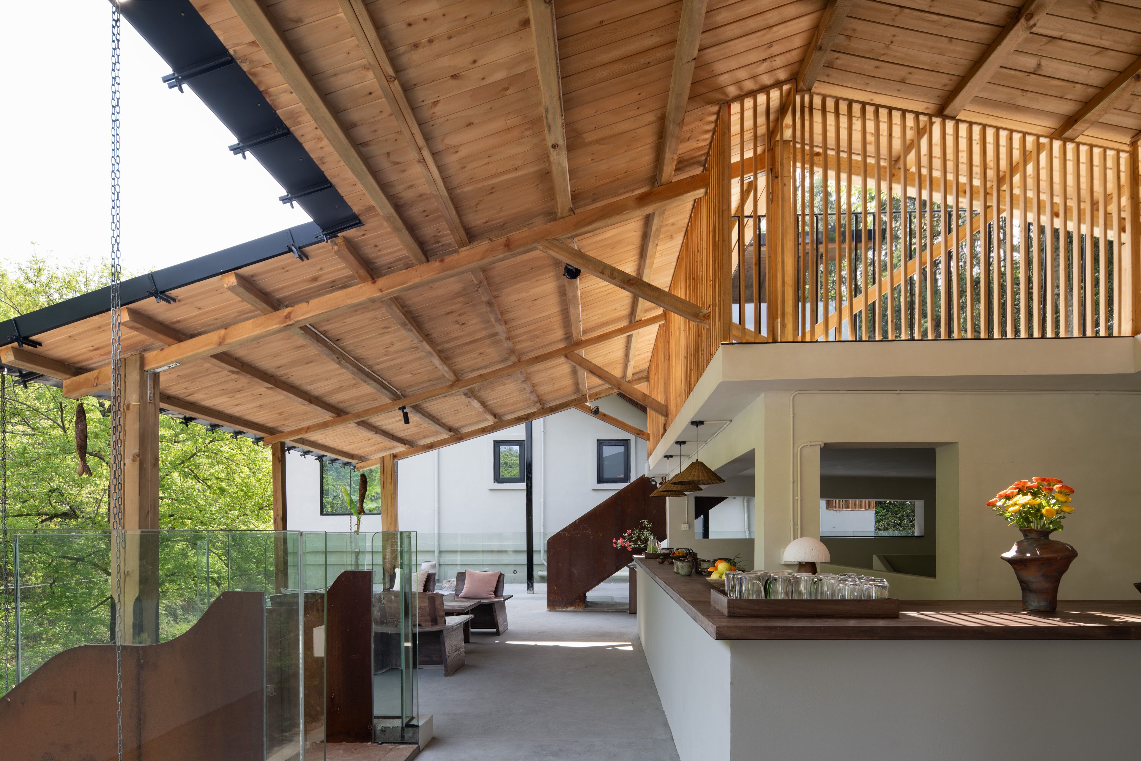 A spacious covered patio area with a wooden ceiling and a glass railing overlooking a garden.