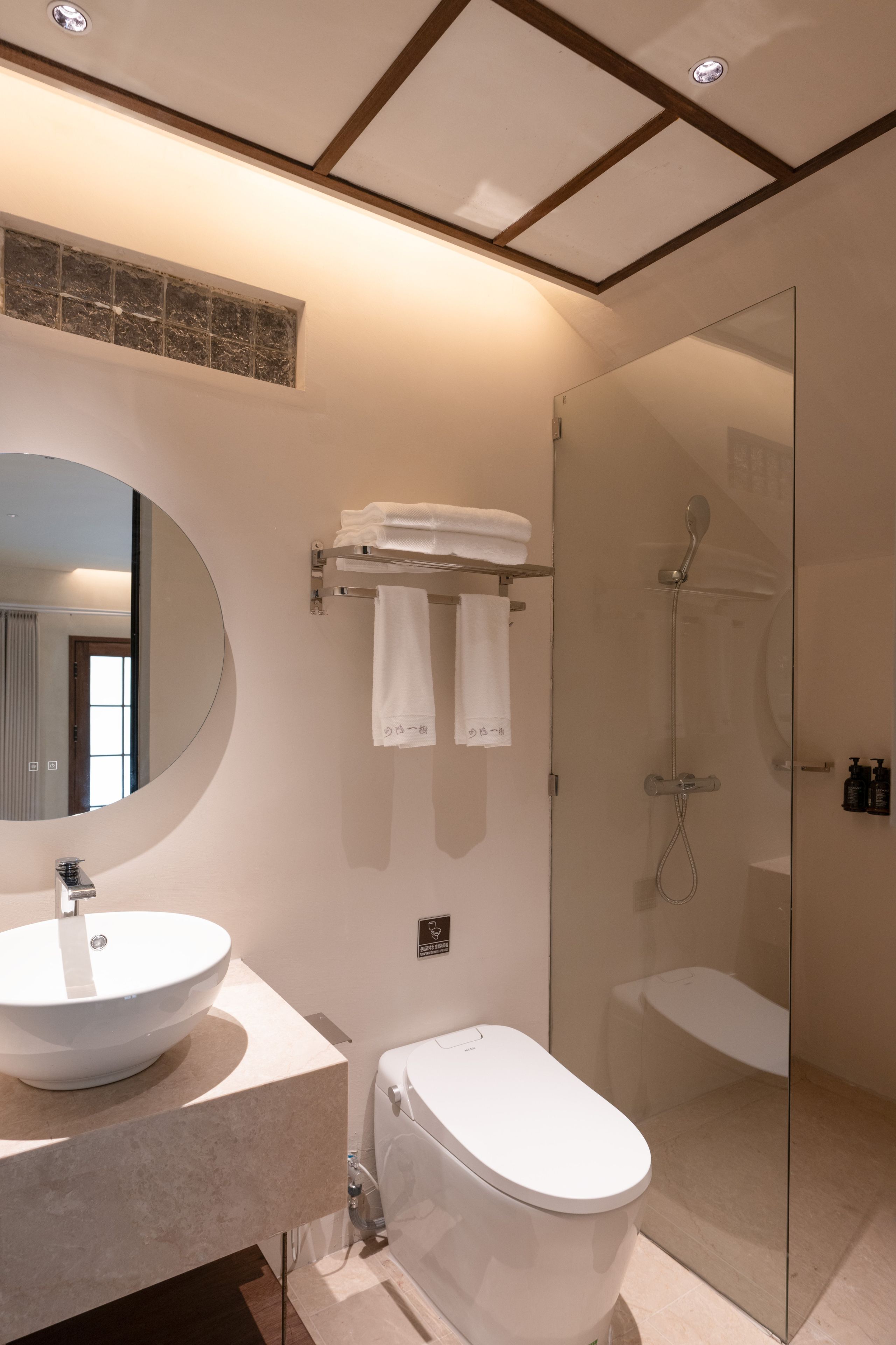 A modern bathroom with a large oval sink, a toilet, and a glass-enclosed shower area.