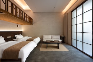 A hotel room with two beds, a sofa, a coffee table, and a large window.