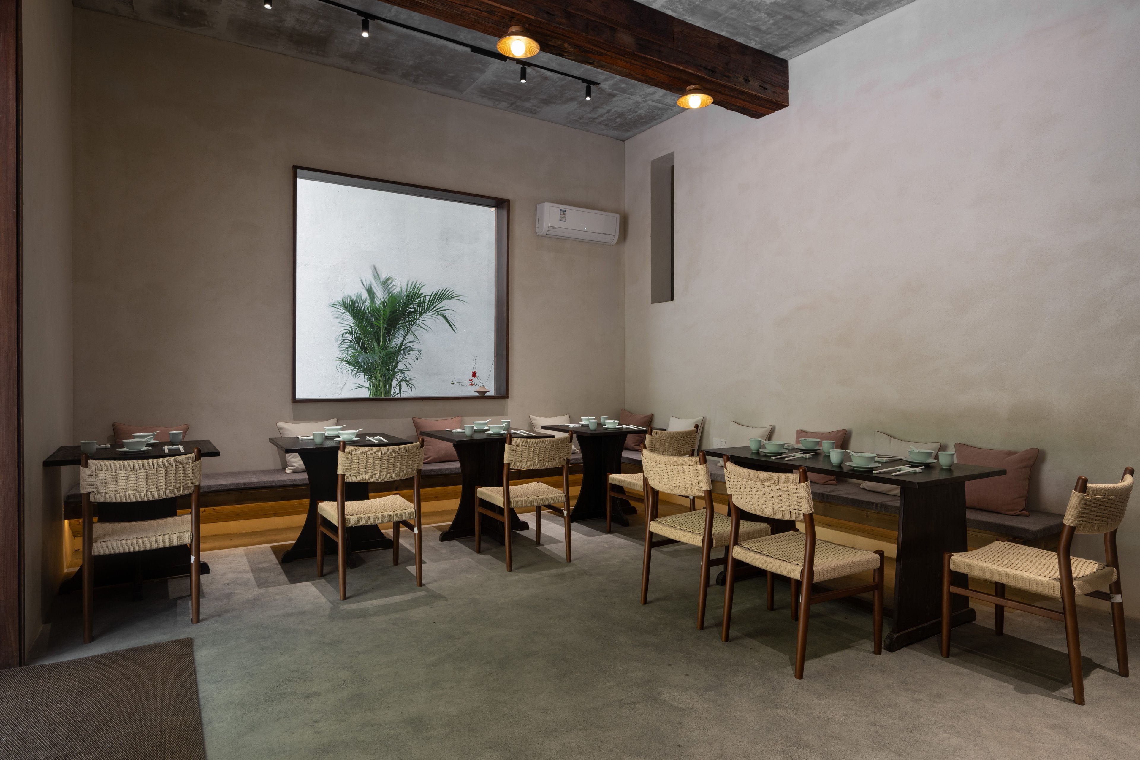 A dining area with multiple tables and chairs, a large window with a view, and a ceiling with exposed beams.