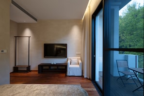 A modern bedroom with a large bed, a TV mounted on the wall, a seating area with a sofa, and a balcony with a table and chairs.