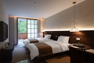 Habitación de hotel con una cama grande, una mesita de noche con lámpara, vista a zonas verdes y cabecero de madera.