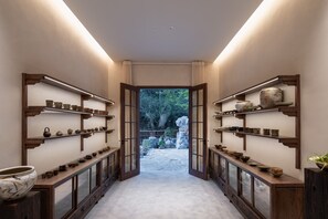 A hallway with shelves displaying various pottery and ceramics, leading to an outdoor garden area.