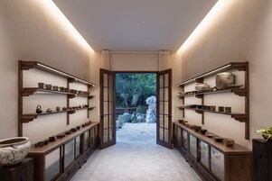 Un pasillo con estanterías que exhiben diversas piezas de cerámica y alfarería, que conduce a un jardín exterior.