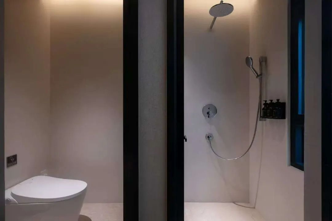 Un baño con inodoro, ducha con cabezal de ducha manual y grifo empotrado en la pared.