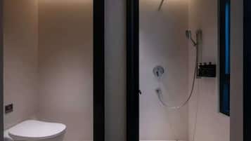 Un baño con inodoro, ducha con cabezal de ducha manual y grifo empotrado en la pared.