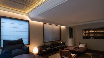 A modern living room with a sofa, a coffee table, a dining table with chairs, a lamp, and a bookshelf.
