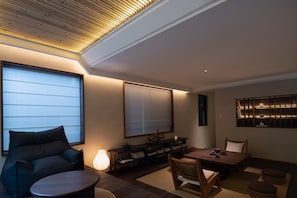 A modern living room with a sofa, a coffee table, a dining table with chairs, a lamp, and a bookshelf.