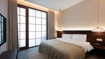 A modern hotel room with a large bed, a bedside table, a desk, and a view through a sliding door.