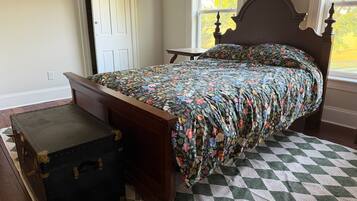 A bedroom with a bed, a chest of drawers, a window, and a door.