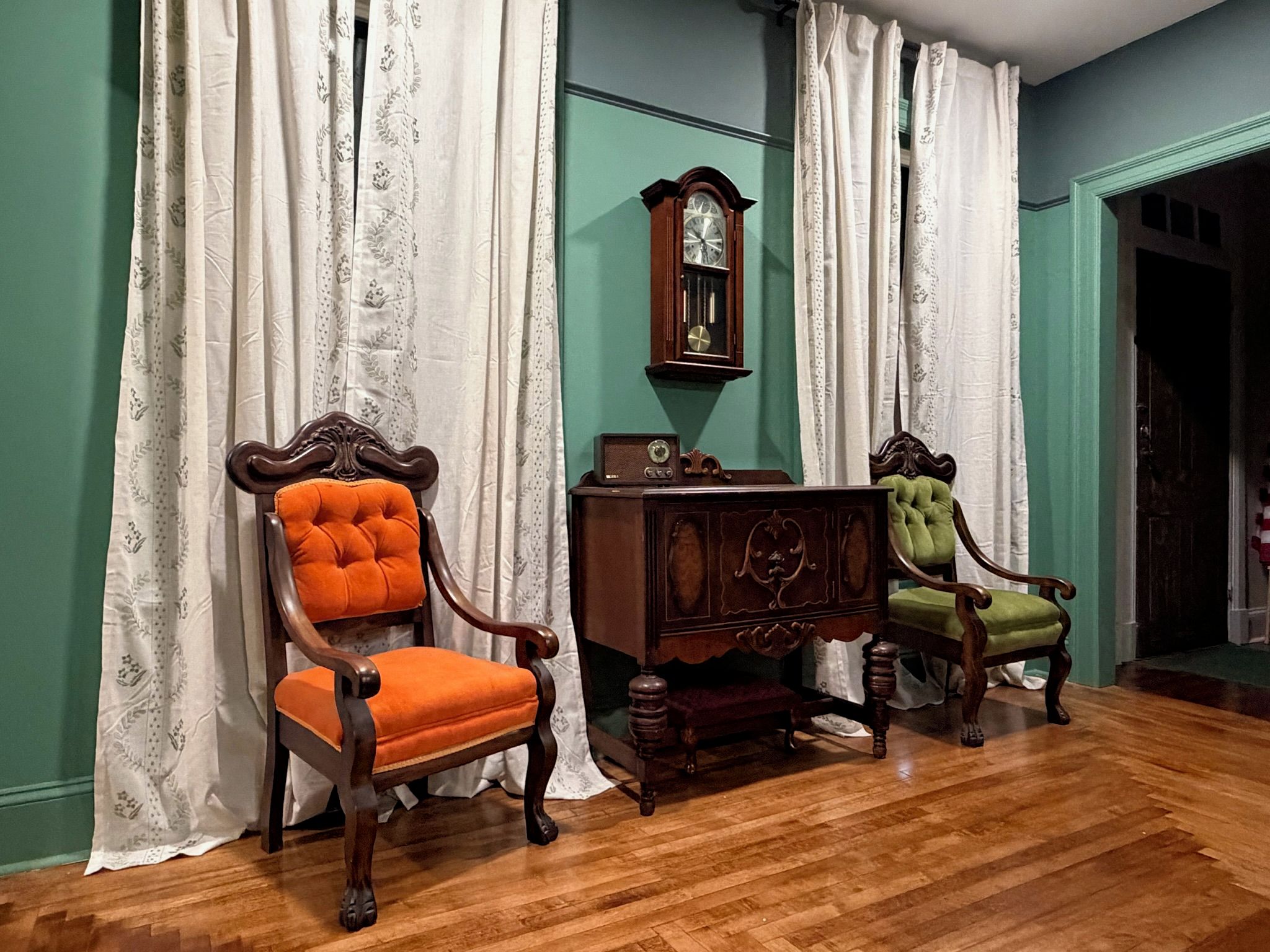 A room with two upholstered chairs, a wooden cabinet, and a wall-mounted clock.