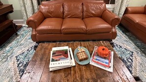 Um sofá de couro marrom em um quarto com cortinas estampadas e uma mesa de centro de madeira com livros e um abóbora.