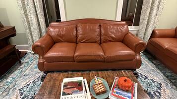 A brown leather sofa in a room with patterned curtains and a wooden coffee table with books and a pumpkin.