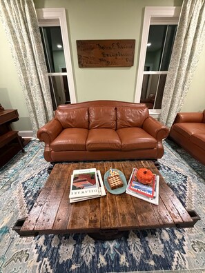 A brown leather sofa in a room with patterned curtains and a wooden coffee table with books and a pumpkin.