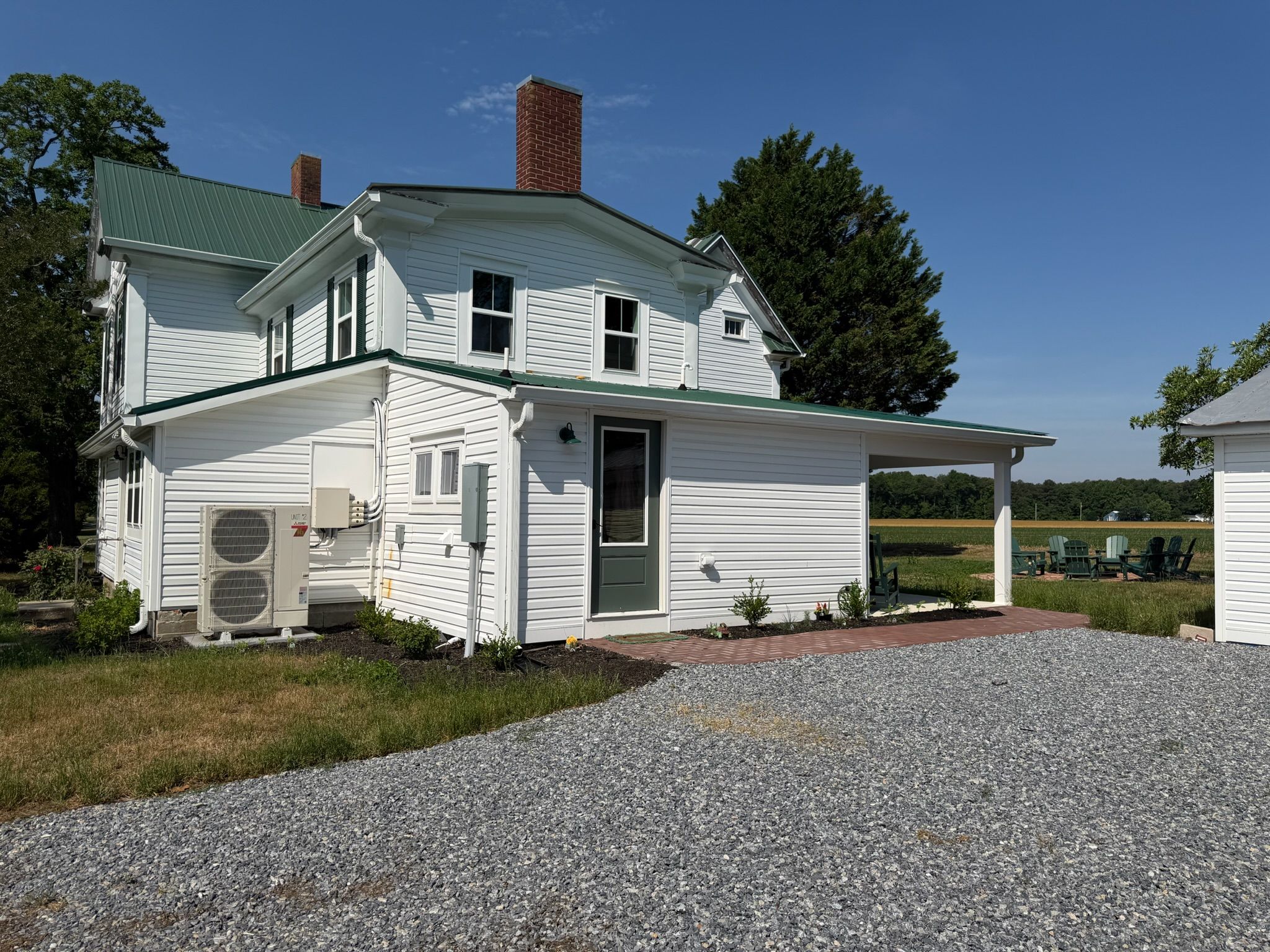 A two-story white house with a green roof, a covered porch, and a gravel driveway.