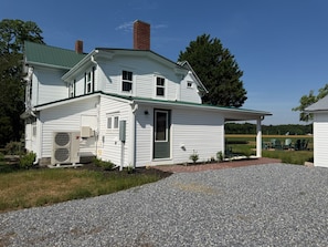 A two-story white house with a green roof, a covered porch, and a gravel driveway.