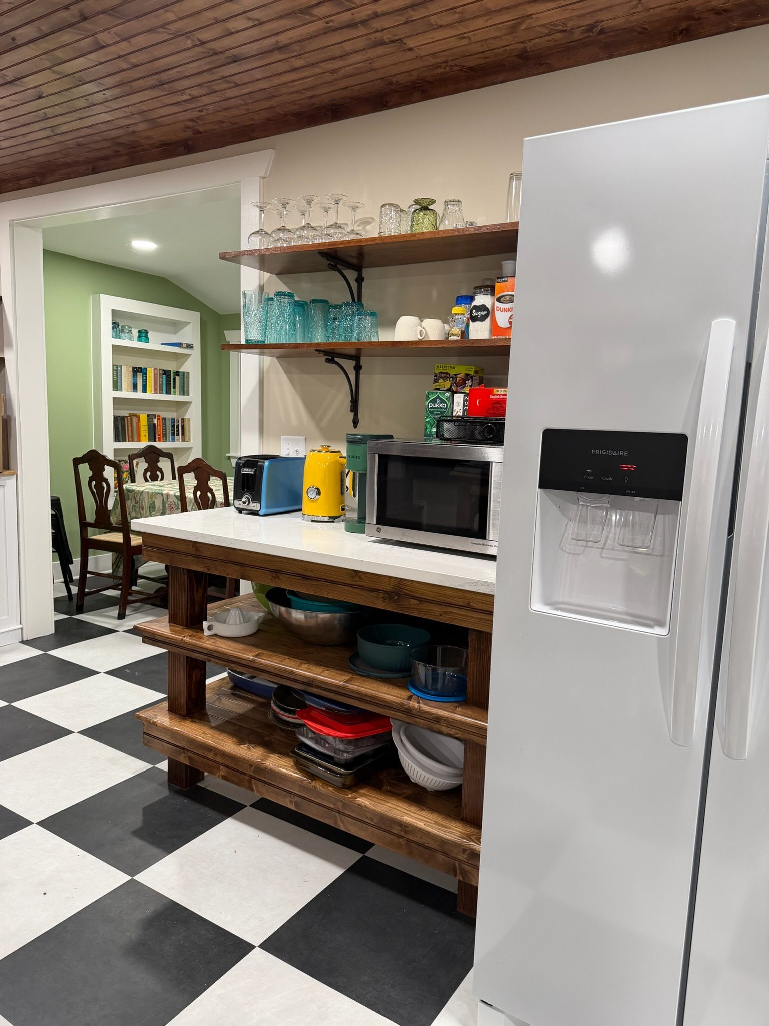 Una cocina con un refrigerador blanco, un microondas, un tostador y un lavamanos. Hay estantes sobre la encimera con diversos utensilios de cocina.