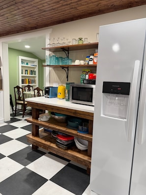 A kitchen with a white refrigerator, a microwave, a toaster, and a sink. There are shelves above the counter holding various kitchen items.