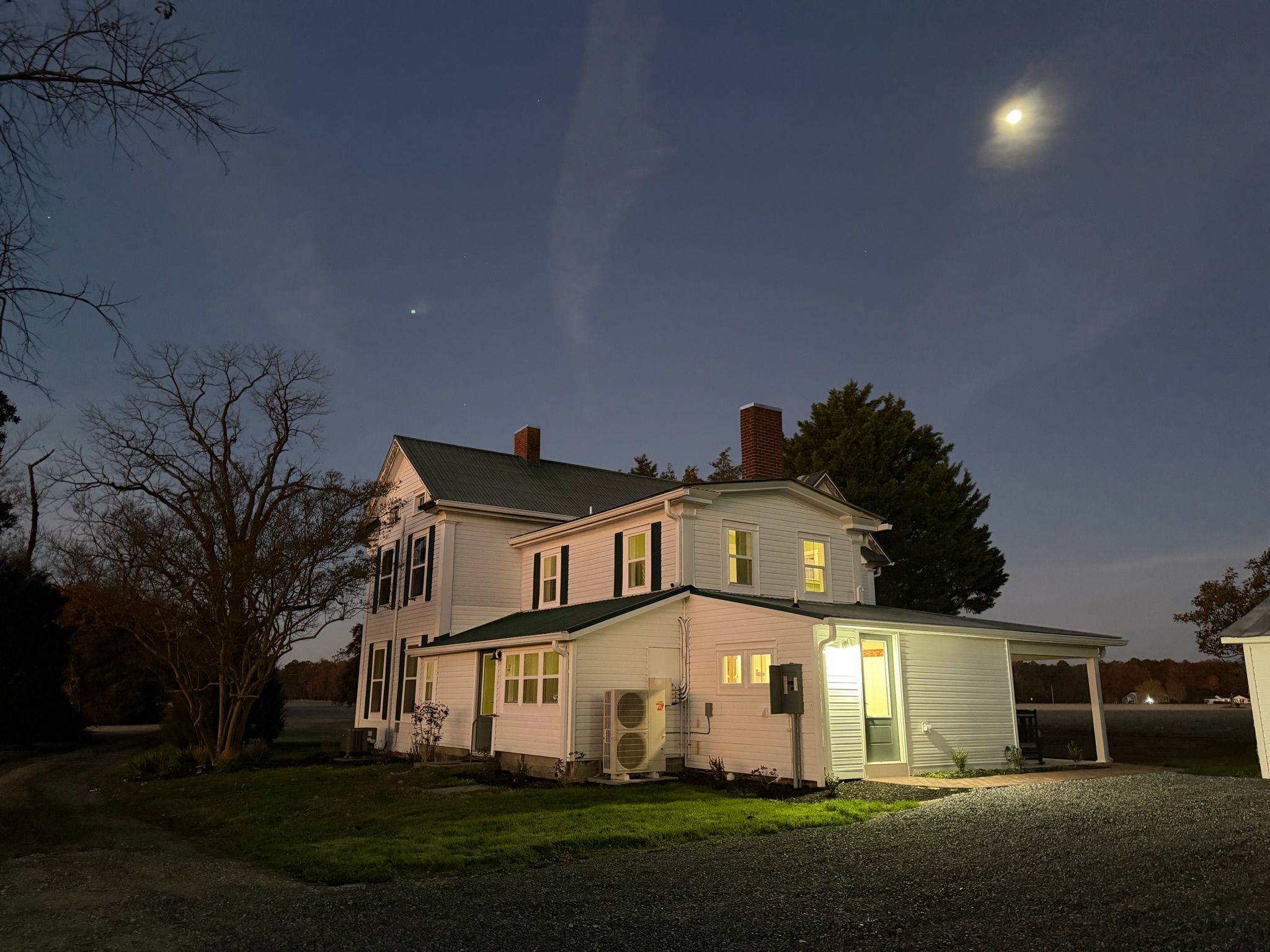 Una casa de dos pisos con un porche, una entrada para vehículos y un cielo nocturno despejado con una luna visible.