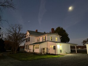 A two-story house with a porch, a driveway, and a clear night sky with a visible moon.