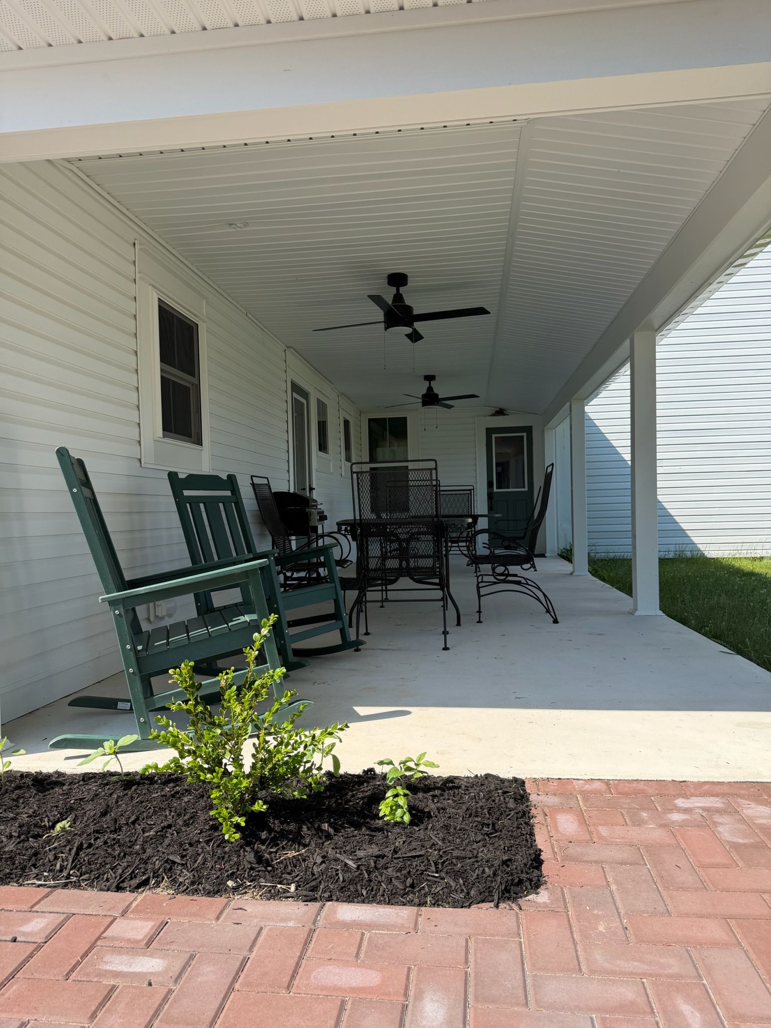 Un patio techado con mobiliario exterior, ventilador de techo y una pequeña jardinera.