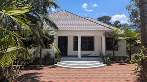 Una casa con techo de tejas, un porche delantero y un jardín con palmeras.