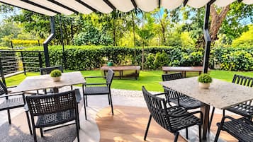 Un patio al aire libre con mesas y sillas, rodeado de follaje y vistas a un jardín bien cuidado.