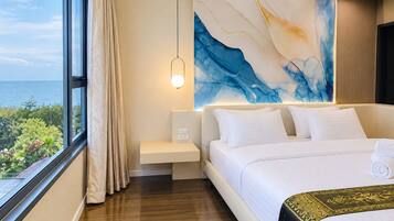 A hotel room with a large bed, a bedside table, a nightstand, a wall-mounted lamp, and a view of the sea.