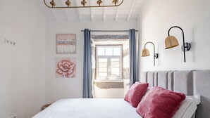 A bedroom with a bed, two pillows, a wall-mounted lamp, and a window with curtains. - Northeast Wind | Basalt Lodge with AC & Jacuzzi and Ocean Views (Lomba da Fazenda)