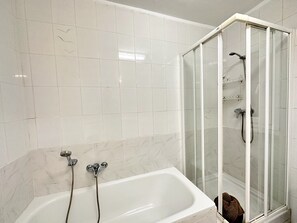 A bathroom with a white bathtub, a glass-enclosed shower, and a marble-tiled wall. - Apartment in Nerja Near Burriana Beach (Nerja)