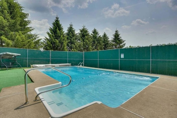 A rectangular swimming pool with a diving board and a ladder, surrounded by a green fence and trees. - Sophisticated Cabin & Suite for Group Retreats in Pleasant Mount, Pennsylvania (Pleasant Mount)