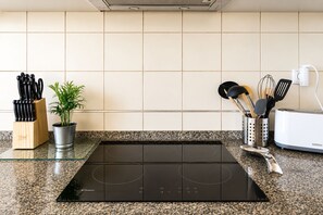A kitchen with a black induction cooktop, a knife block, a potted plant, and a toaster. - Dolly Monte Verde - Apartment with Ocean View (Faro)