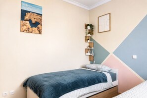 A bedroom with a bed, a wall-mounted shelf with plants, a painting, and a geometric wall design. - Dolly Monte Verde - Apartment with Ocean View (Faro)