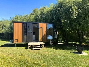 A modern, compact cabin with a wooden exterior, a small deck, and a picnic table.