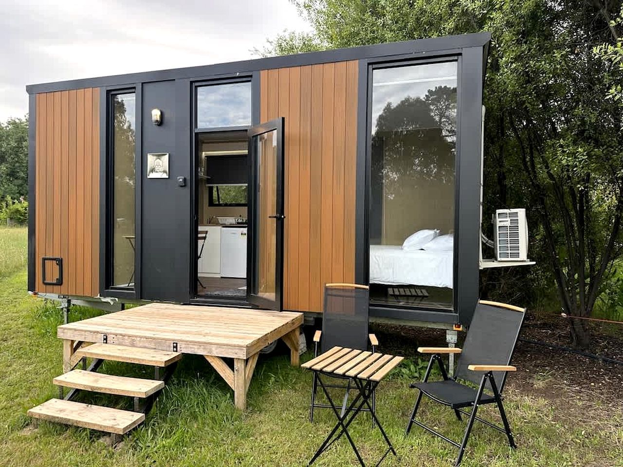 A modern, compact mobile home with a dining area, a bed, and a small kitchenette.