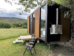 Ein modernes, kompaktes Wohnmobil mit Schiebetür, einer kleinen Terrasse mit Tisch und Stühlen sowie einer Klimaanlage.