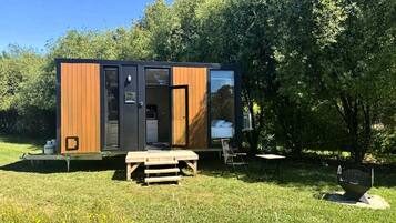 A modern, compact cabin with a wooden exterior, a small deck, and a picnic table.