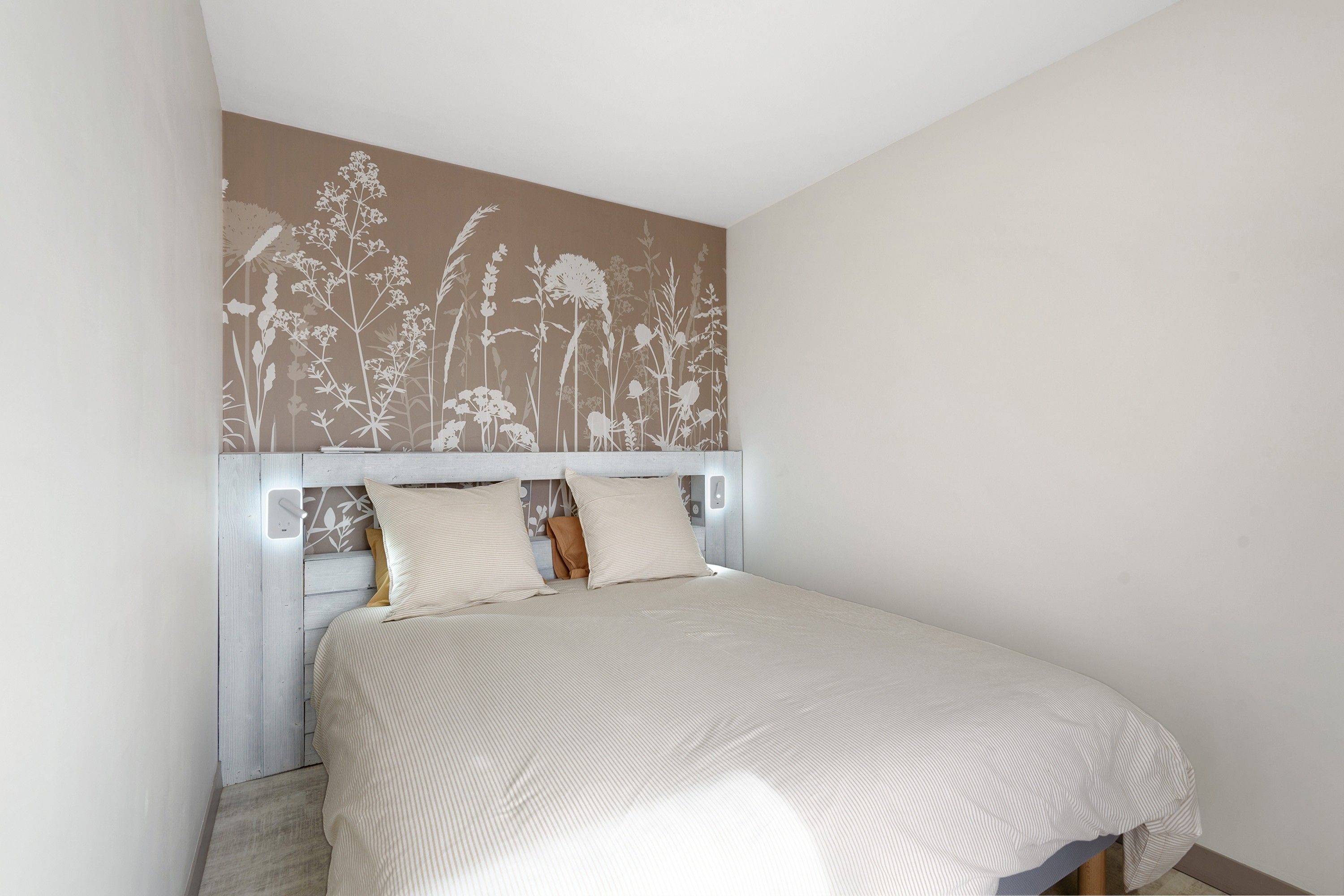 A bedroom with a bed, a headboard, and a wall with a floral pattern.