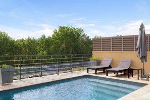 En pool på taket med solstolar och en pergola.