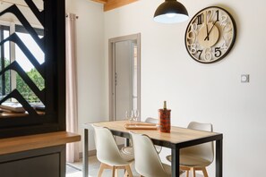 En matplats med ett träbord, vita stolar, en väggklocka och ett fönster med utsikt över grönområden.